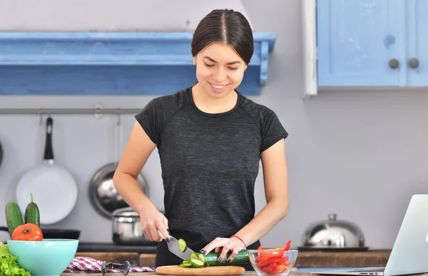 Photo of young asian woman smiling while cooking salad with fresh vegetables in kitchen interior at home.