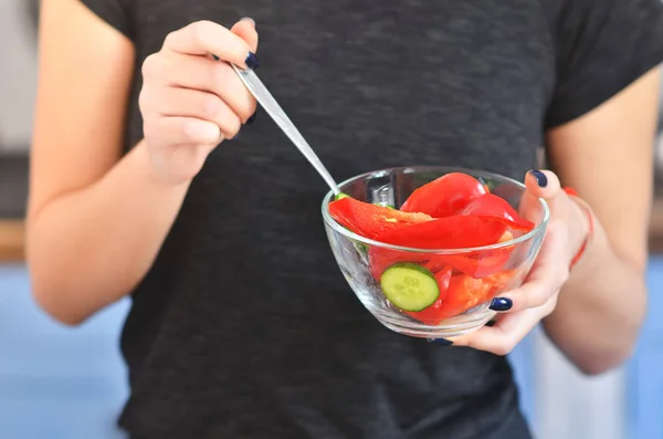 Una giovane ragazza con una t-shirt nera mescola il pepe rosso nella ciotola in cucina. Piatto con pepe sullo sfondo . Fotografia Stock