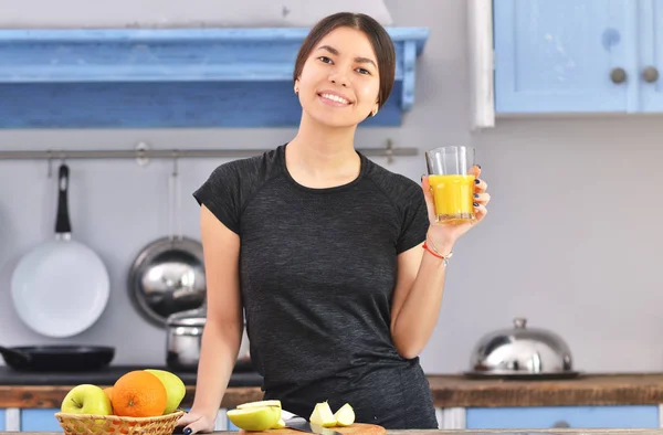 Genç bir Asyalı fitness kızı evde bir bardak portakal suyu yapıyor..