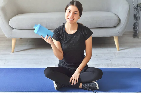 Fitness girl, home and diet concept - smiling teenage girl sitting on mat with sports equipment at home