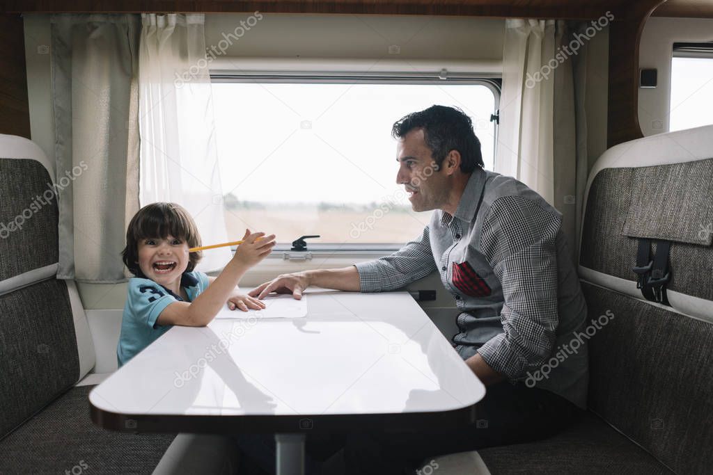 Father and son with the holiday caravan, performing school work
