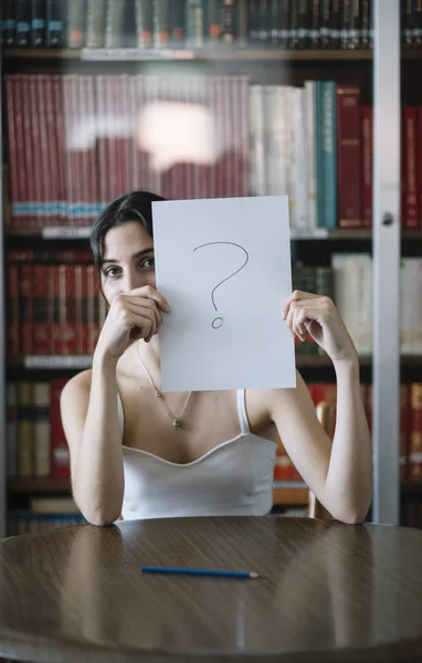 view of a young woman studying in the table on a library with mark of interrogation on a leaf