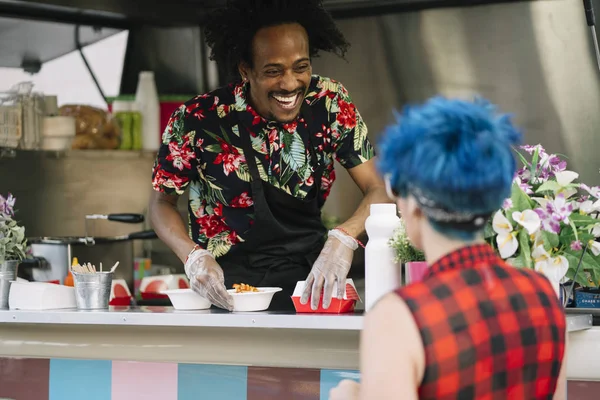 Smiling food vendor hands food to waiting customer