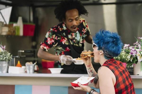 Smiling food vendor hands food to waiting customer