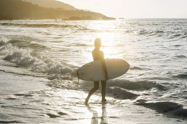 Sörf tahtası ayakta okyanus, ıslak kum plajındaki kadınla.