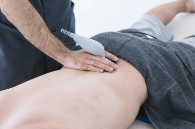 Radyo terapisi için ekipman kullanan bir adamı tedavi eden fizyoterapist.