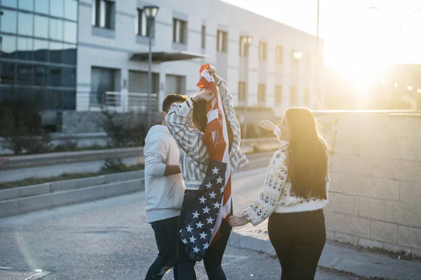 Sokaklarda Amerikan bayrağı taşıyan bir grup mutlu arkadaş.