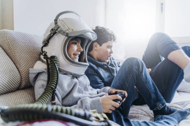 Kanepede yatan ve evde bir video oyun konsolu ile oynayan iki çocuk