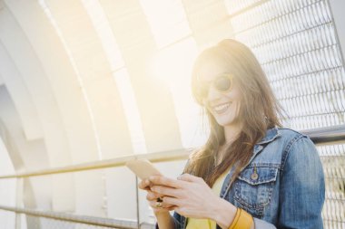 Sokakta yürüyen mutlu kadın akıllı telefon içeriğini kontrol ediyor.