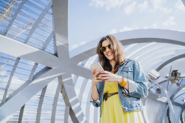 Woman wearing yellow shirt texting on the smart phone walking in the street in a sunny day