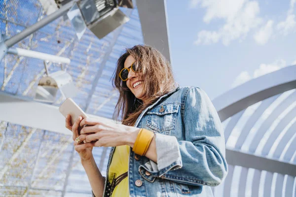 Donna che indossa camicia gialla sms sullo smart phone a piedi per strada in una giornata di sole — Foto Stock