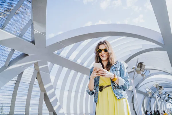 Woman wearing yellow shirt texting on the smart phone walking in the street in a sunny day