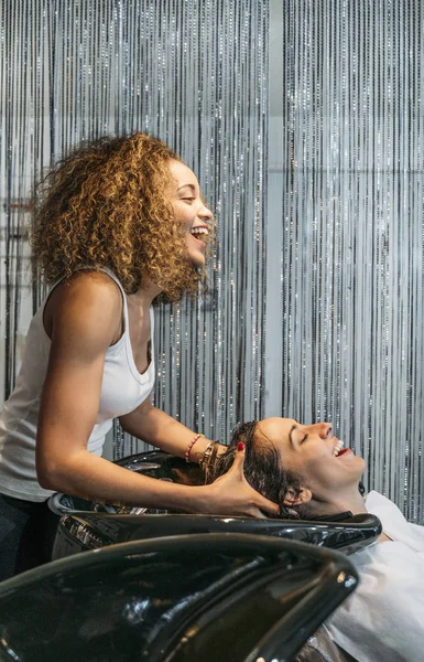 Афро-стиліст миття волосся привабливої леді біля раковини в перукарні — стокове фото