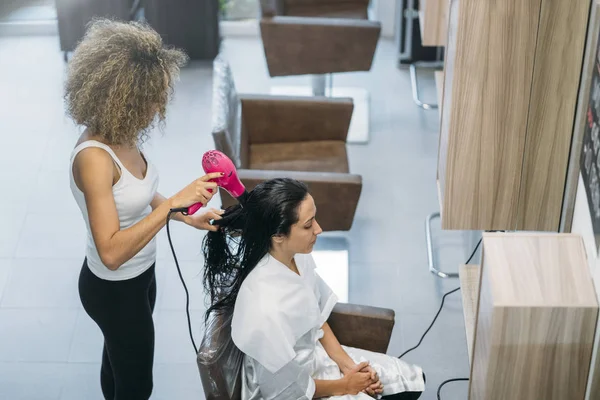 Primer plano de una peluquera alisando el pelo largo morena con planchas de pelo . —  Fotos de Stock