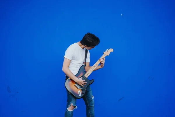 Jovem com guitarra elétrica no fundo azul — Fotografia de Stock
