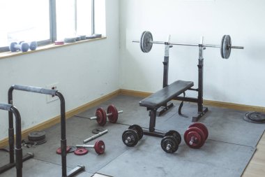 Spor salonunda güneş ışığı alan bir ağırlık alanı. Ağırlık yığınları ile çevrili bir kilo tezgah var.