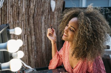 Elleri dudaklarına yakın genç ve güzel bir bayanın yansıması kuaförde aynaya bakıyor.