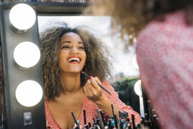 Elleri dudaklarına yakın genç ve güzel bir bayanın yansıması kuaförde aynaya bakıyor.