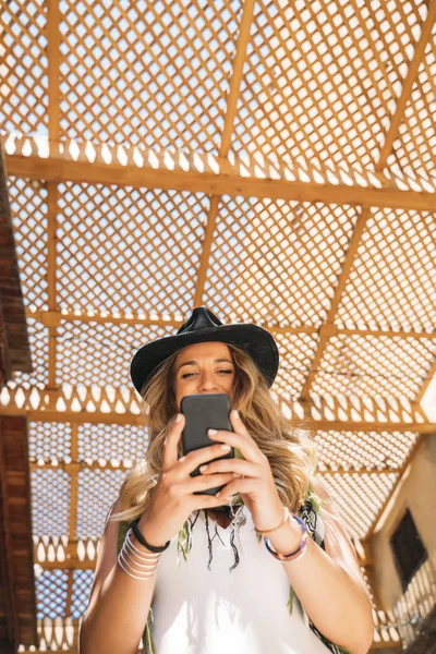 Mulher usando chapéu preto mensagens no telefone inteligente na rua — Fotografia de Stock