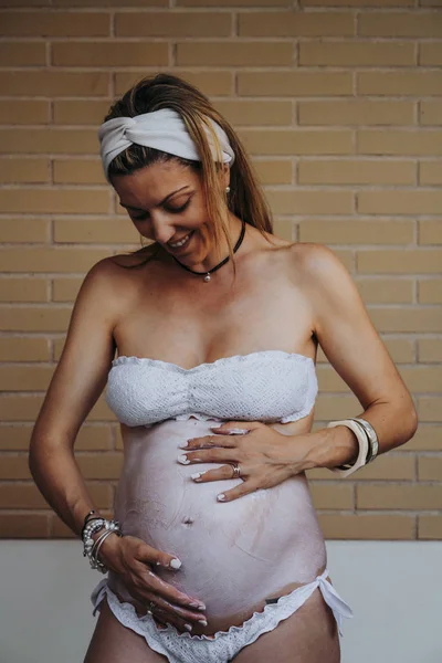 Közelkép a terhes nő hasa krém alkalmazása — Stock Fotó