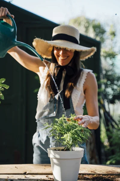 Wanita tersenyum menyiram tanaman di kebun — Stok Foto