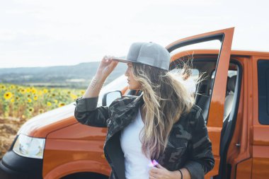 Turuncu minibüsün dışında şapkalı hoş bir sarışın kadın.