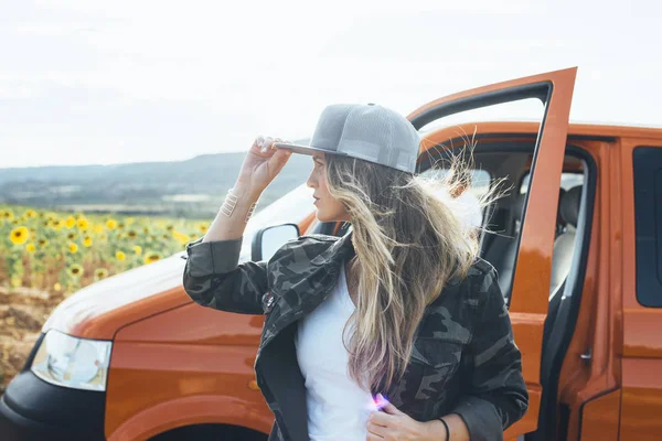 Miła blondynka z czapką na zewnątrz pomarańczowy van — Zdjęcie stockowe