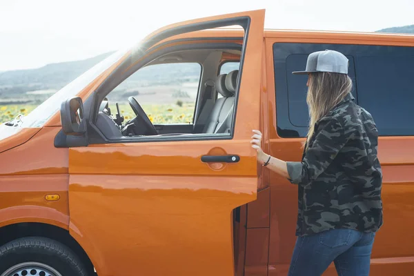 Çölde genç bir kadın minibüs kapısı açık duruyor.