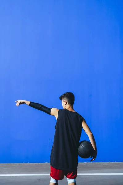 Back view of a man holding a basket ball in front of blue wall — Stock Photo, Image