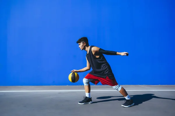 Man playing basketball in front of a blue wall — Stock Photo, Image