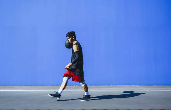 Man playing basketball in front of a blue wall. — Stock Photo, Image