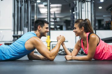 Spor salonunda yerde yatarken bilek güreşi yapan iki sporcu.