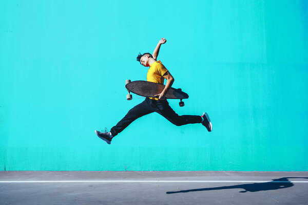 Skater Boy jumping with longboard in the colorful street