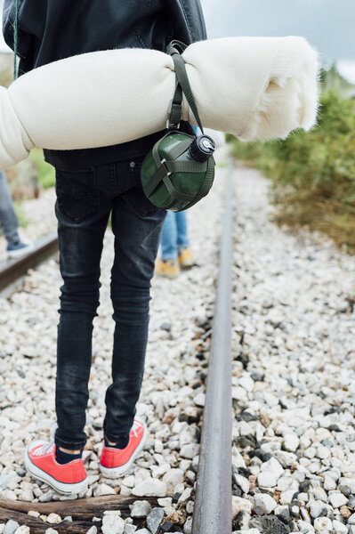 Kid hiking in the woods caring a sleeping bag walking in a train track with water bottle
