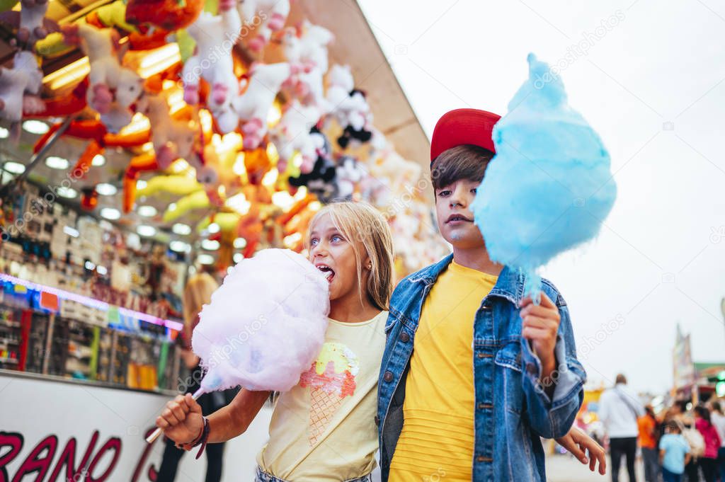 Boy and girl eating sweet cotton at the amusement park