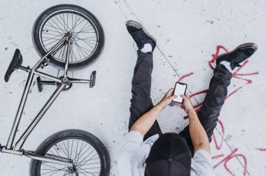Yukarıdan Bmx sürücüsü zemin duvarında akıllı telefonuyla dinleniyor.