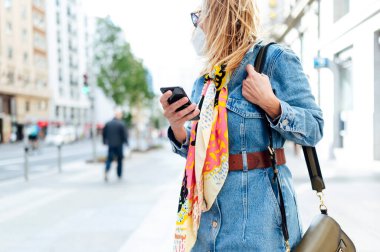Sokakta cep telefonu kullanan bir kadın. Virüsü önlemek için koruyucu bir maske takıyor. Coronavirus konsepti