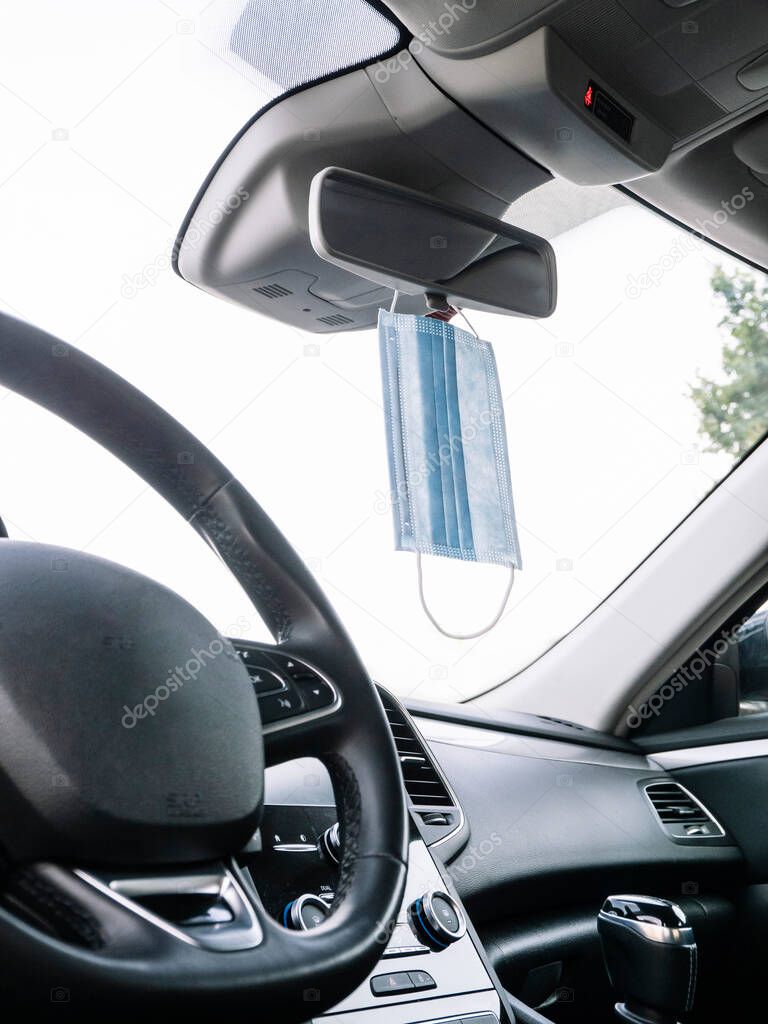 Protective face mask hanging from a car's rear view mirror.