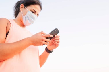 Atletik kadın dışarıda yüz maskesi takan akıllı telefonunu kullanıyor.