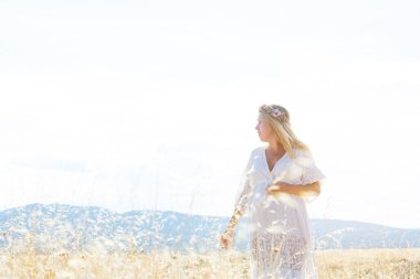 Kırsal çayırda duran hamile, beyaz kadın.