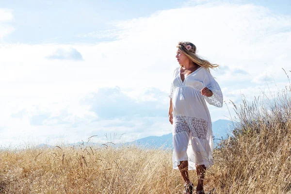 Kırsal çayırda duran hamile, beyaz kadın.