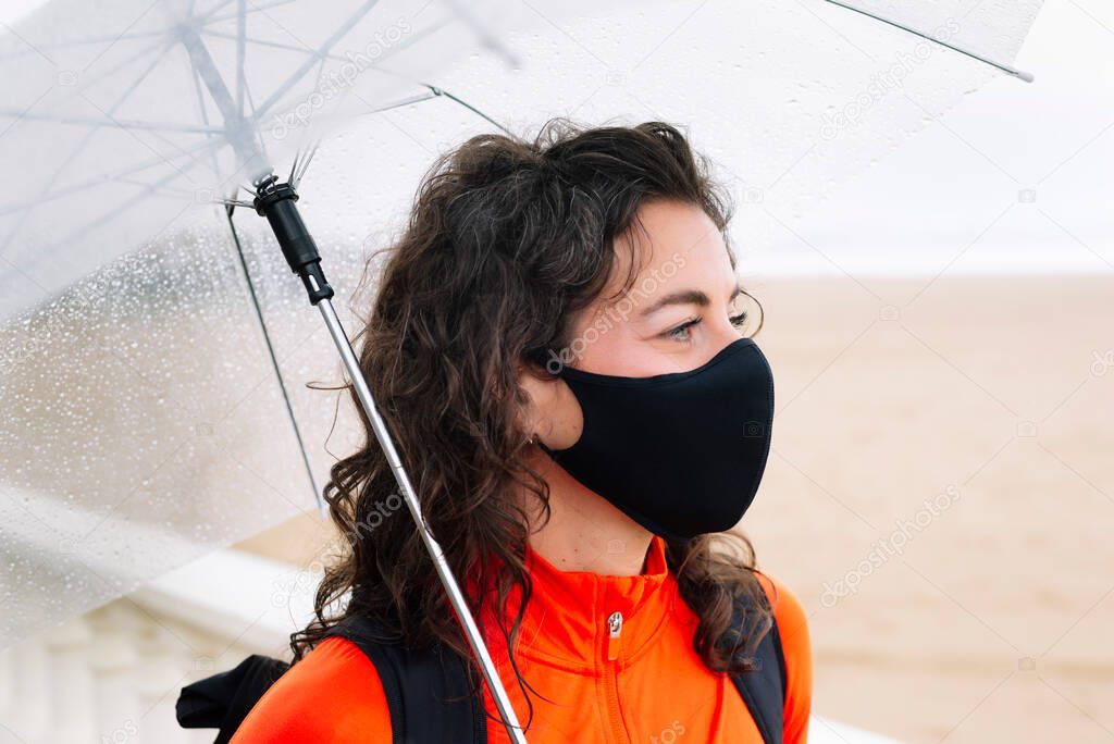 Athletic woman with mask and umbrella down the street