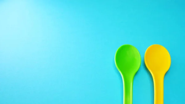 Yellow and green plastic spoons at green background isolated