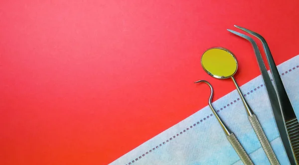 Diş hekimi araçları veya diş Office Araçları: diş keşfe çıkmak, orak sonda, diş ayna ve cerrahi veya yordam yüz maskesi, kırmızı bir arka plan. Dişlerle ilgili sağlık bilgisi ve sağlık kavramsal görüntü
