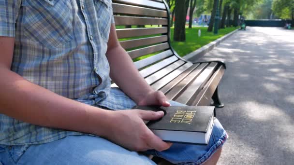 Ember a Szent Biblia tart a kezében, ül egy padon a parkban, a nyári időszakban egy napsütéses napon