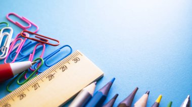 Kalem, kurşun kalem, cetvel, ataç ve marker masanın üzerinde. Okul üzerinde mavi arka plan sağlar. Yukarıdan kopya alanı ile göster