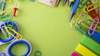 Okul üzerinde yeşil arka plan sağlar. Kalem, kurşun kalem, makas, cetvel, ataç, defter ve marker masanın üzerinde. Yukarıdan kopya alanı ile göster