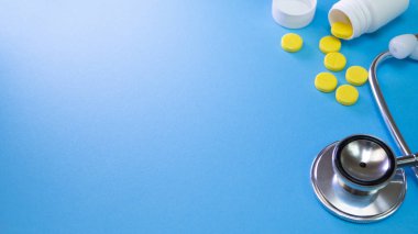 Tıp stetoskop kalp için doktor muayenesi ve sarı hap hap hastane veya mavi arka plan eczanede masada beyaz şişe plastik ile