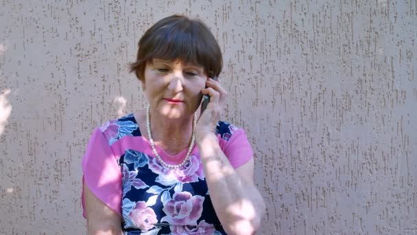 Senior vrouw praten over telefoon buiten in de omgeving van huis — Stockvideo