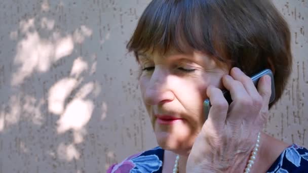 Senior vrouw praten over telefoon buiten in de omgeving van huis — Stockvideo